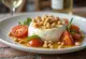 Kavrulmuş çam fıstıklı burrata, taze domates ve marul ile servis edilmiş.